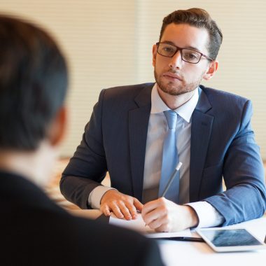 Closeup of serious middle-aged business man sitting at desk and interviewing unrecognizable applicant who is sitting back to camera in office